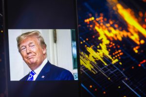 A smartphone screen displaying a photo of President Donald Trump, with a stock chart in the background, symbolizing the his impact of crypto market or XRP value